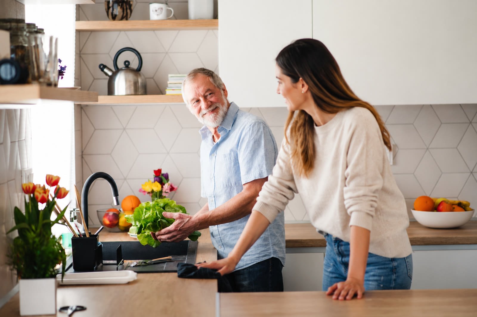 An older man and a younger woman preparing fresh food together in a bright kitchen